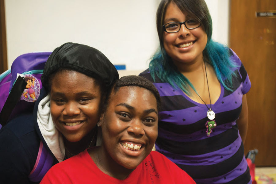 Three cheerful young students posing for a photo, with two girls in the foreground and one partly behind them