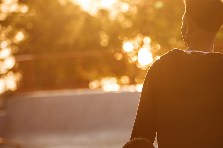 Black teenager with skateboard standing in the sun